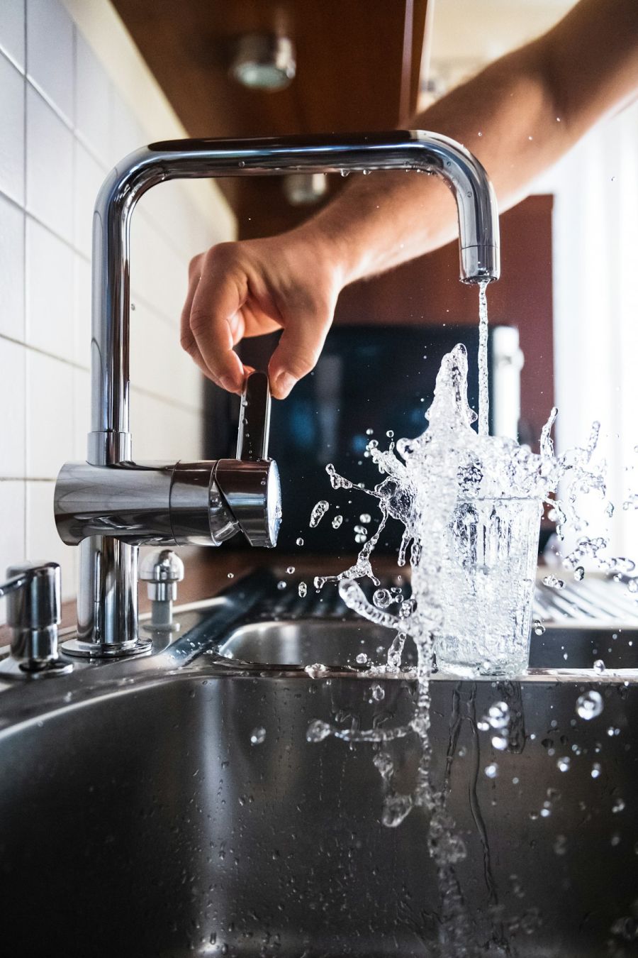 Running kitchen faucet with water splashing into a glass