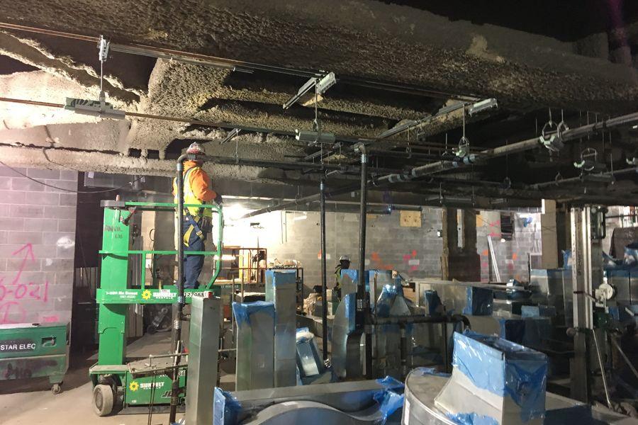 Contractor on a lift installing overhead HVAC ductwork in a building under construction