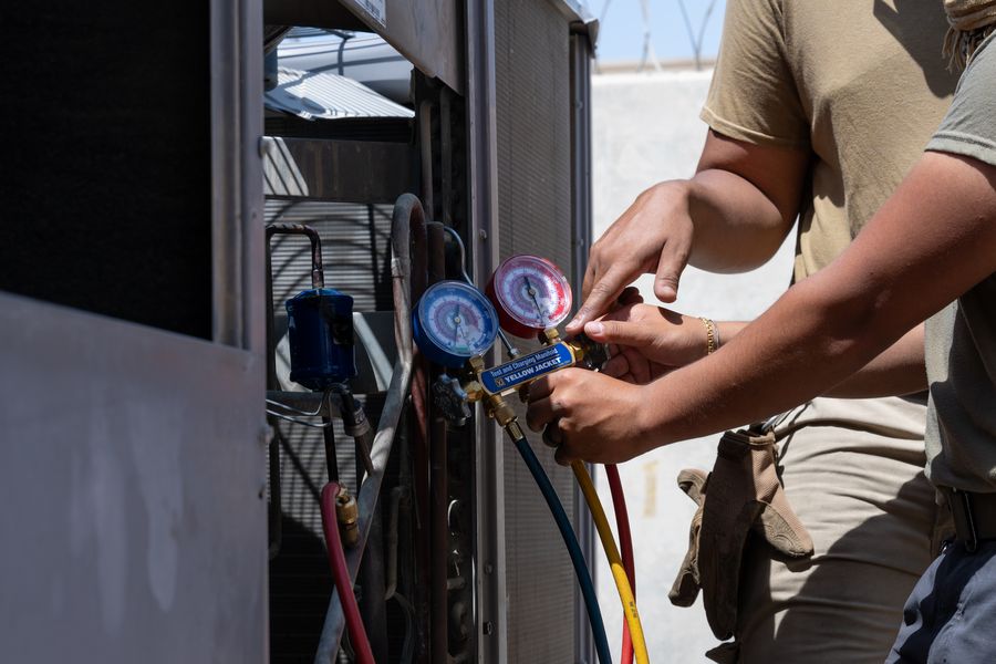 Technician checking refrigerant pressures on an air-conditioning unit with manifold gauges