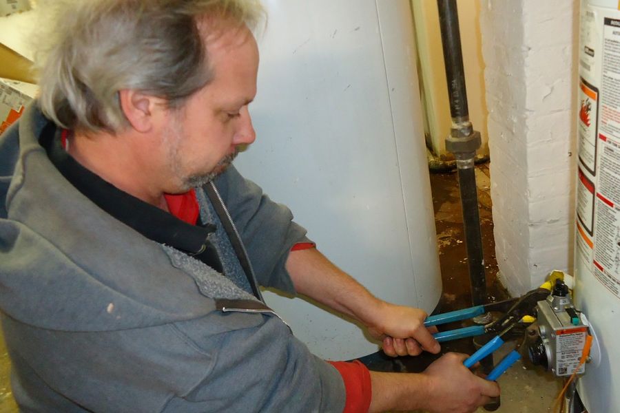 Plumber tightening a fitting at a water heater with two wrenches
